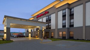 Un moderno Hampton Inn con entrada cubierta, estacionamiento y cielo despejado.