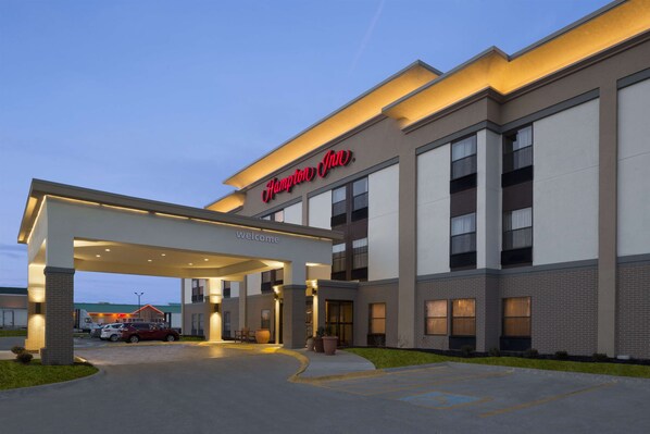 A modern Hampton Inn with a covered entrance, a parking lot, and a clear sky.