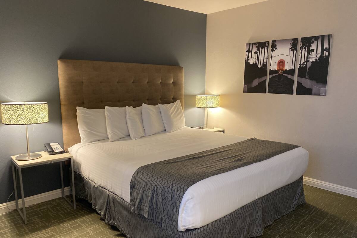 A neatly made bed with a grey and white bedspread, two bedside lamps, a telephone, and a framed picture on the wall.