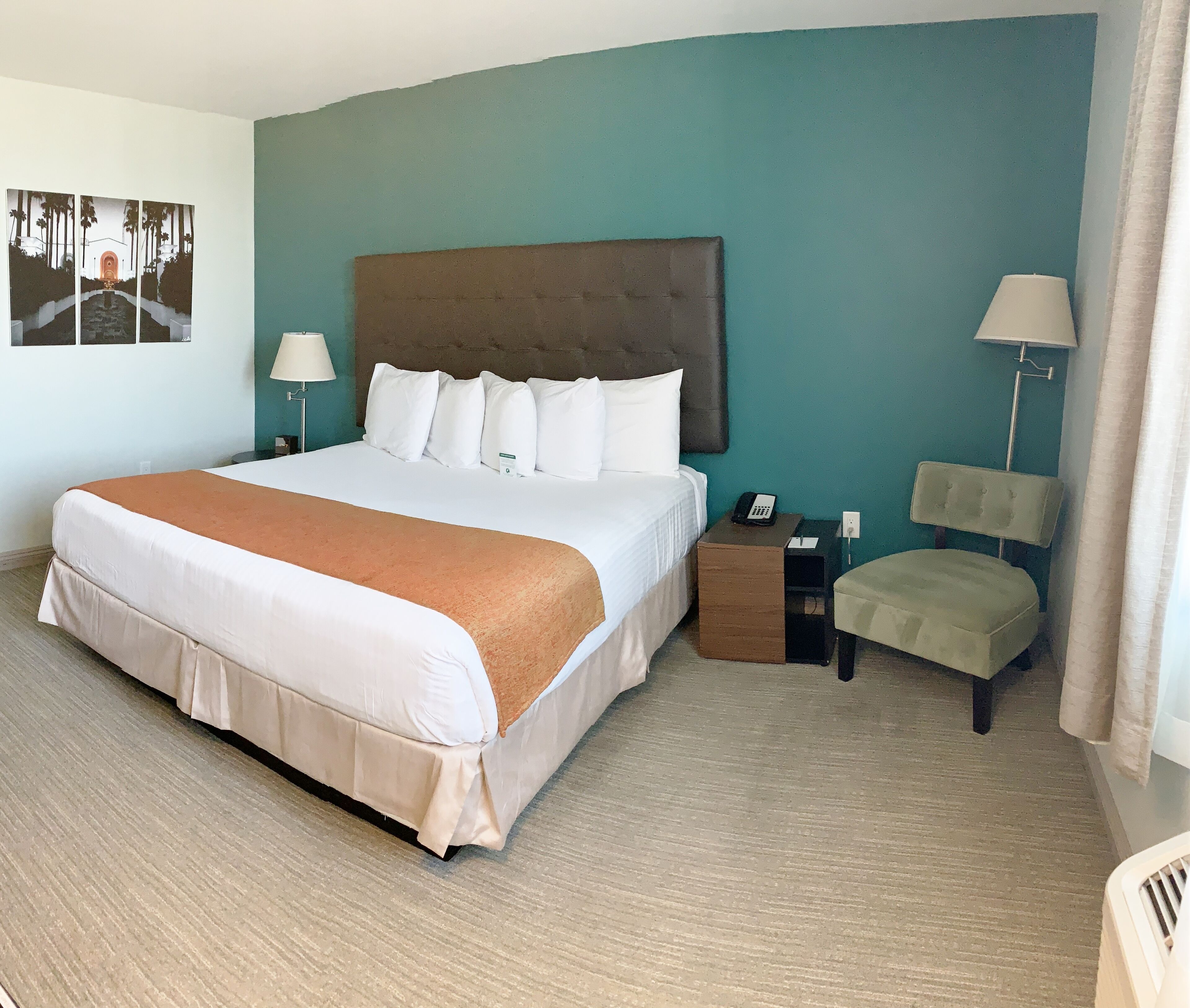Ein Hotelzimmer mit einem großen Bett, einem Nachttisch, einem Sessel und einem fest montierten Telefon.