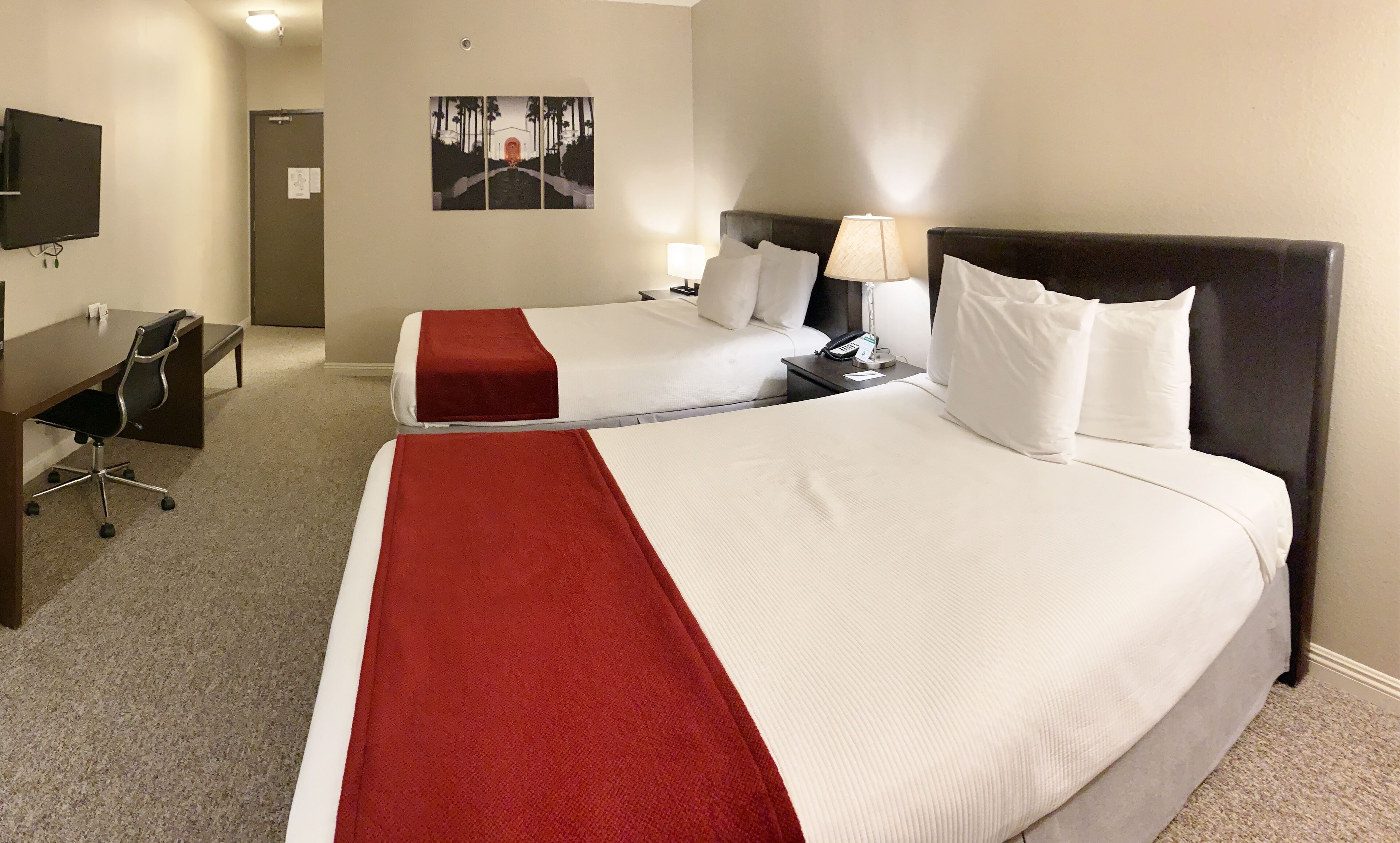 Una habitación de hotel con dos camas, un escritorio, una silla y un televisor en la pared.