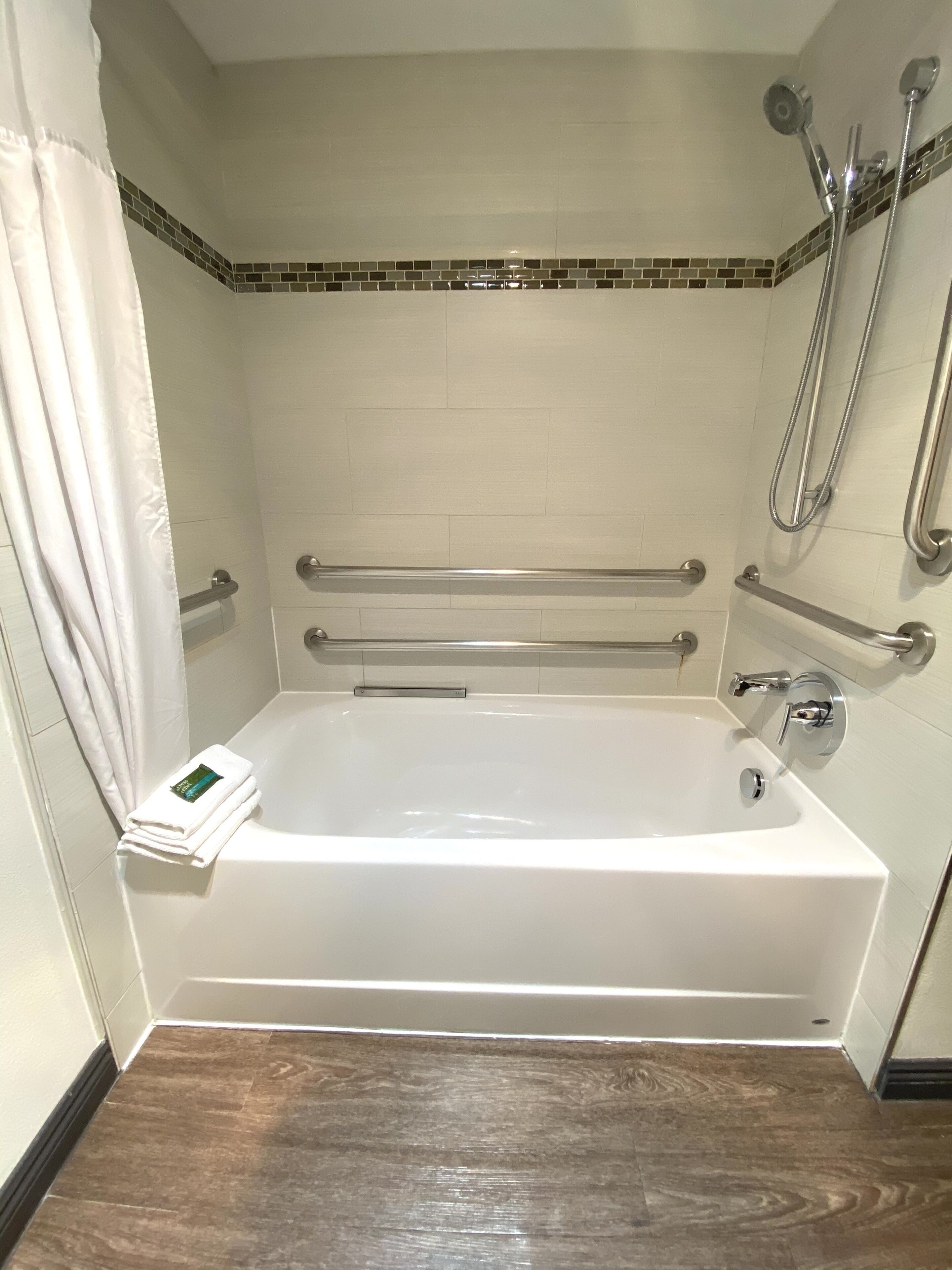 Un baño con una bañera blanca, barras de apoyo, un cabezal de ducha y un perchero para toallas.