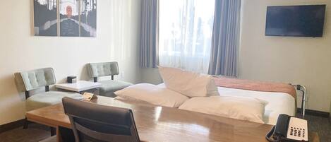 A hotel room with a bed, a desk, two chairs, a telephone, and a painting on the wall.