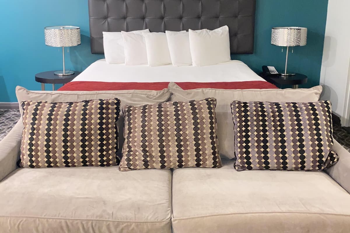 A hotel room with a bed, two bedside tables with lamps, a beige sofa, and a blue accent wall.