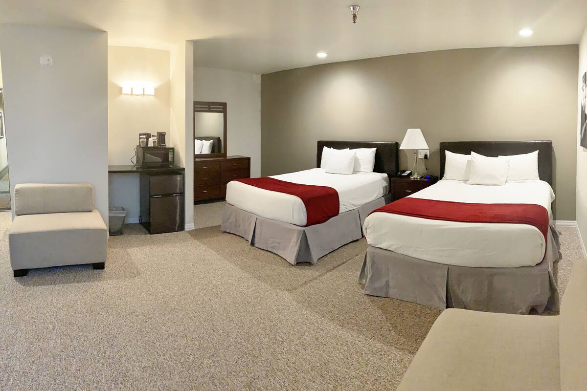 A hotel room with two beds, a desk, a chair, and a small kitchenette.