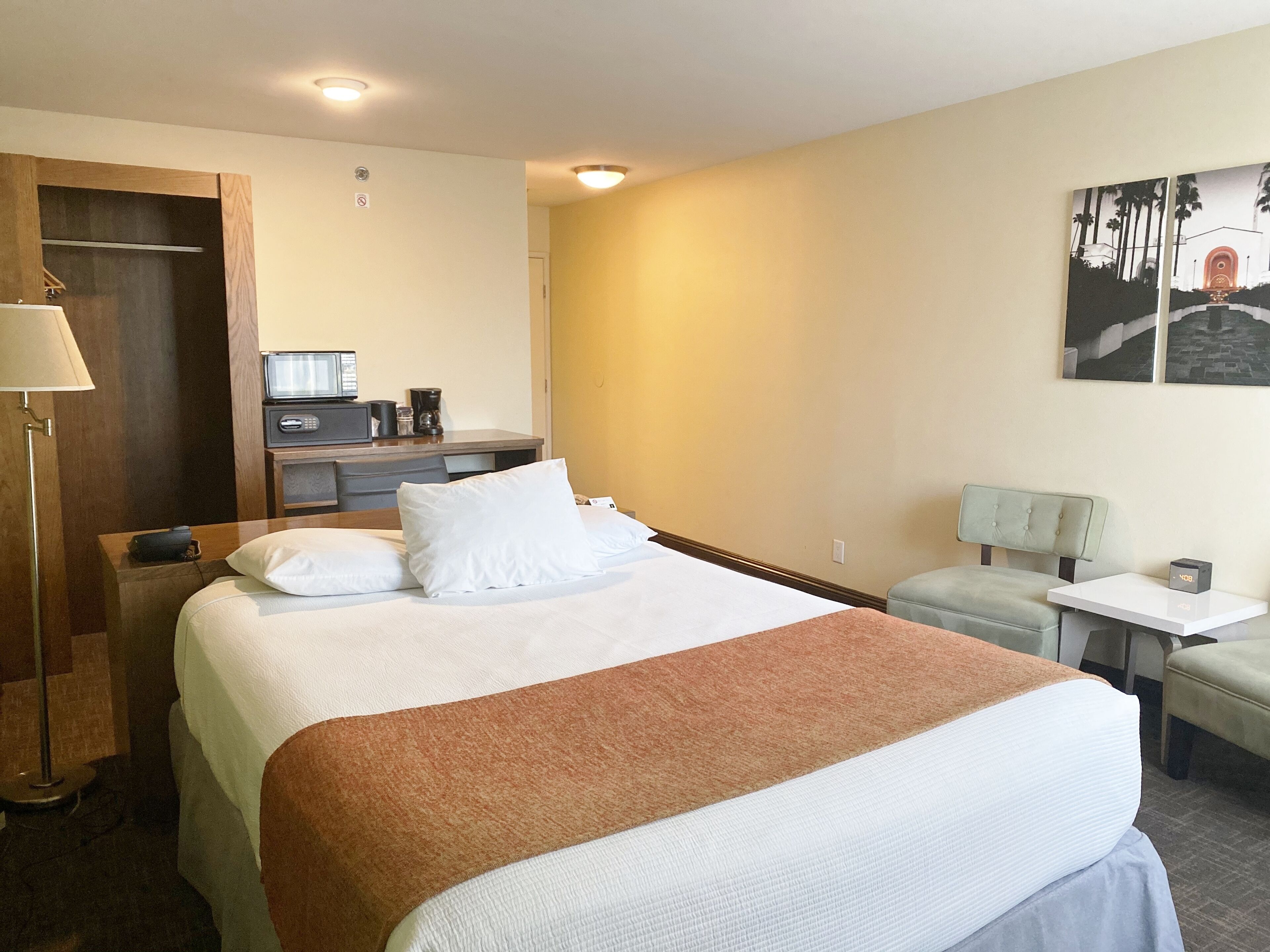 A hotel room with a large bed, a desk with a computer, a coffee maker, and a small table with a lamp.