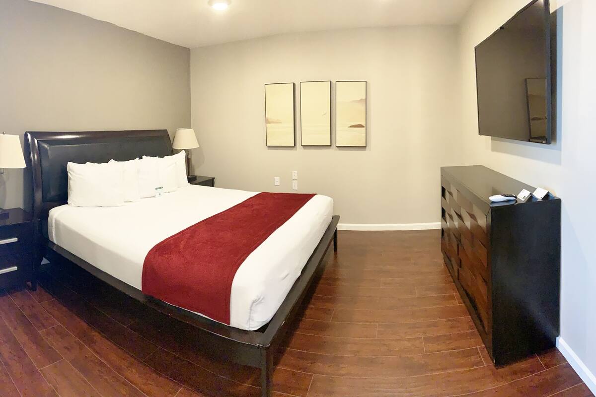 A hotel room with a bed, a dresser, a mirror, and two wall-mounted paintings.