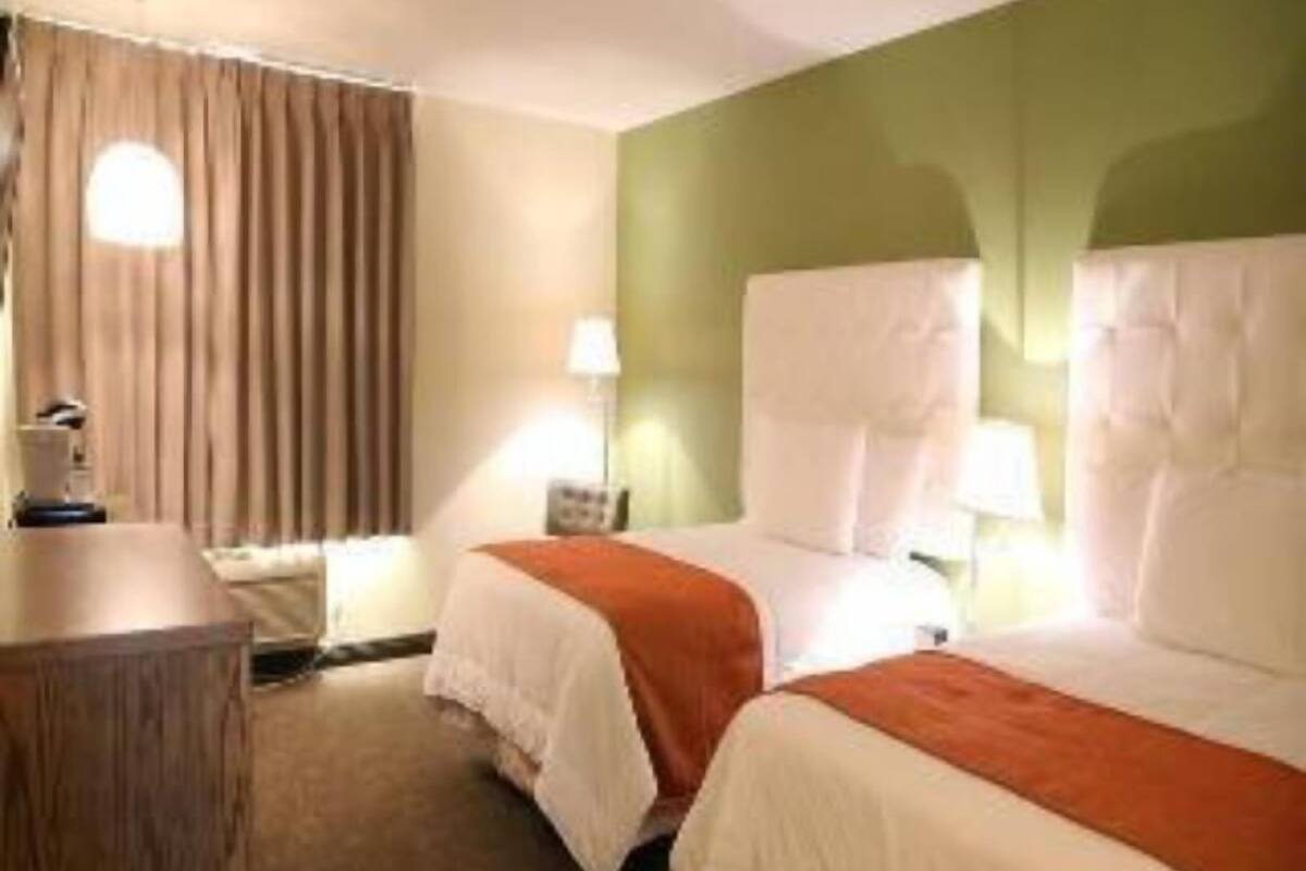 A hotel room with two beds, a desk, and a lamp.
