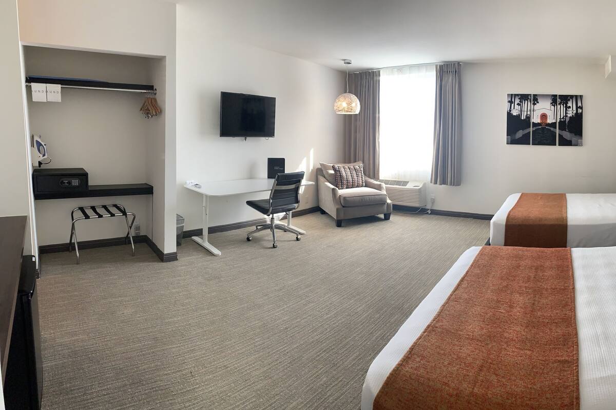 A hotel room with two beds, a desk, a chair, a TV, and a painting on the wall.
