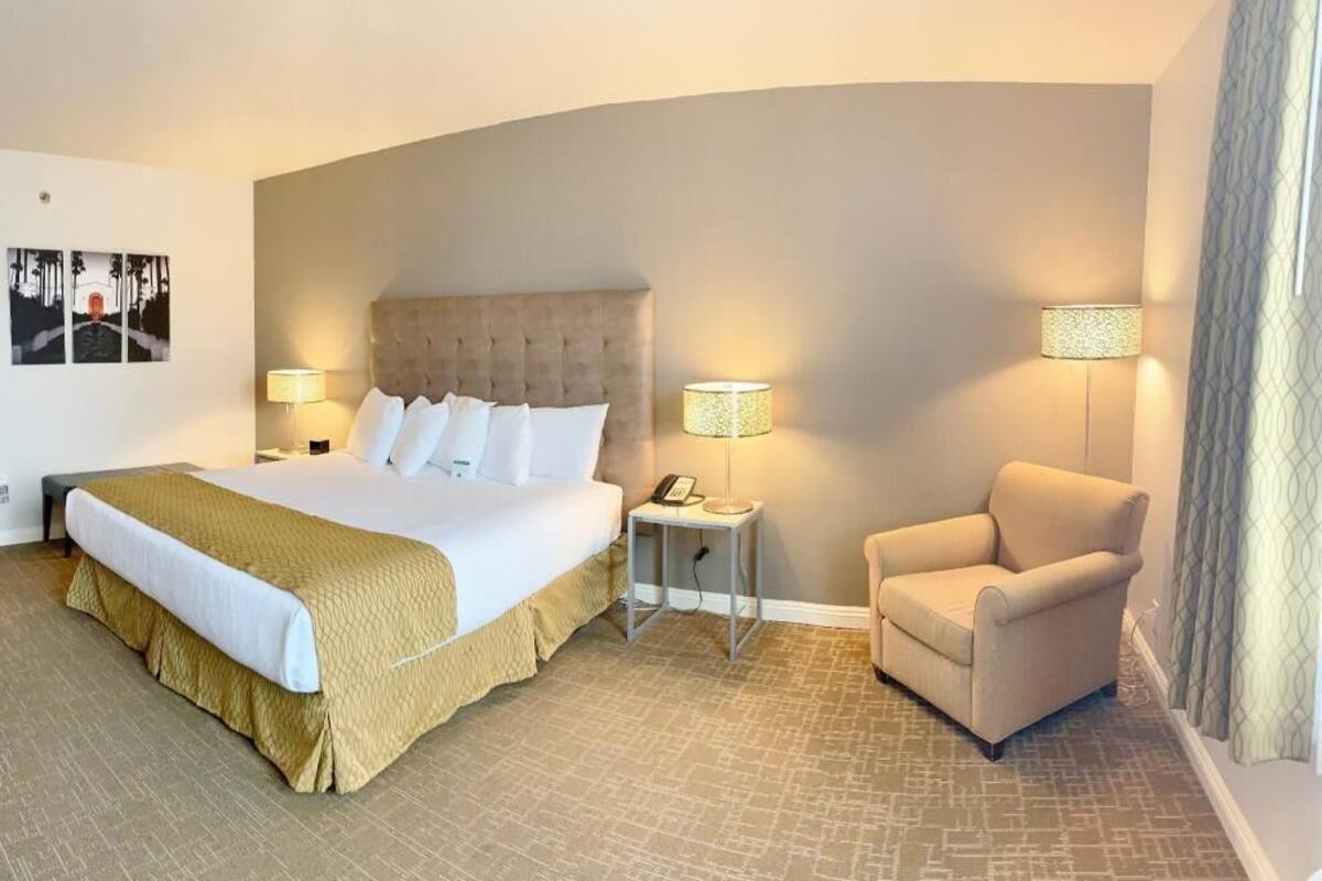A hotel room with a large bed, two bedside lamps, a chair, and a small table.