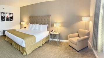 Una habitación de hotel con una cama grande, lámparas de noche, una silla y una mesita.