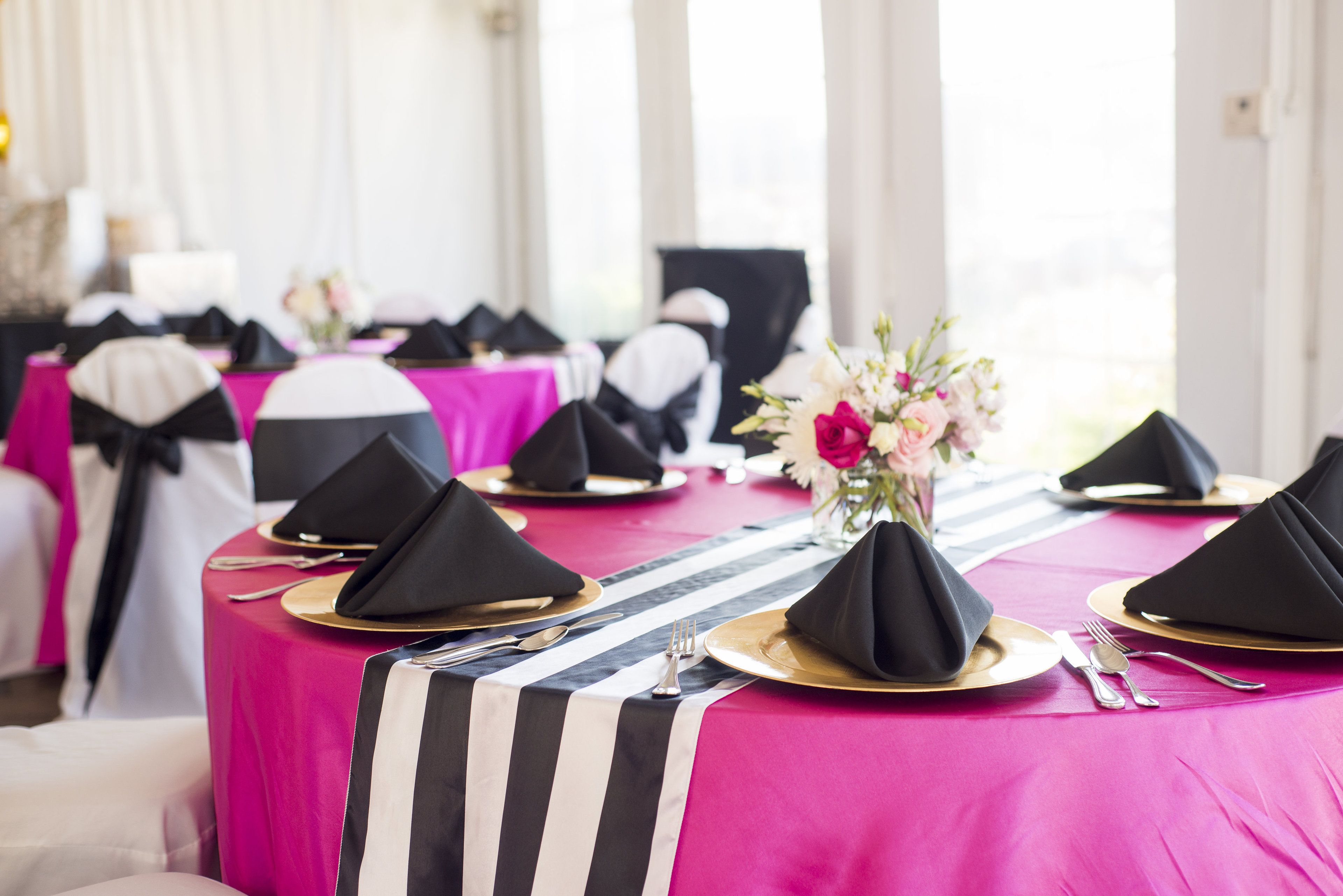 A table set with black napkins, gold plates, and a striped table runner.