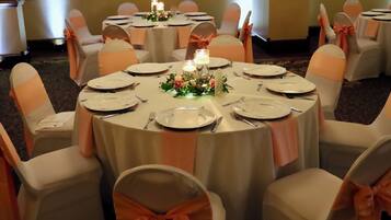 Une table ronde dressée pour un événement formel, avec des nappes blanches, des chaises assorties et des centres de table floraux.
