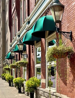 A row of red brick buildings with green awnings and hanging flower baskets. - The Blennerhassett, a Giovanni Hotel and Spa (Parkersburg)