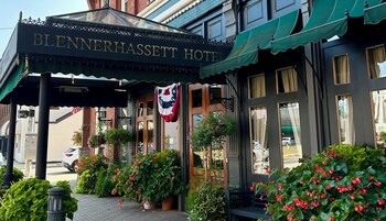 Entrada do Hotel Blennerhassett com varanda coberta, plantas em vasos e uma bandeira.