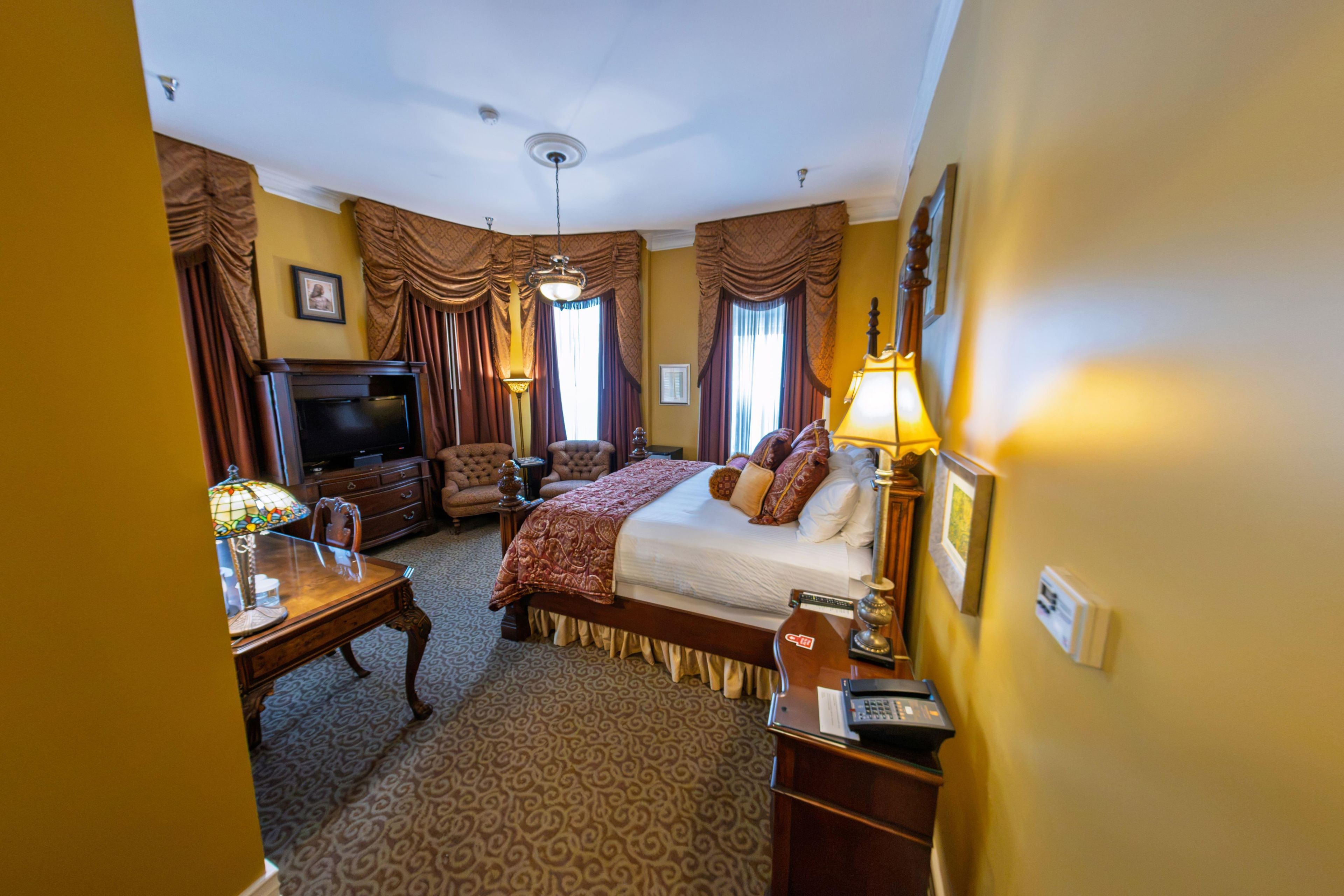 A hotel room with a bed, a desk, a television, and a lamp.