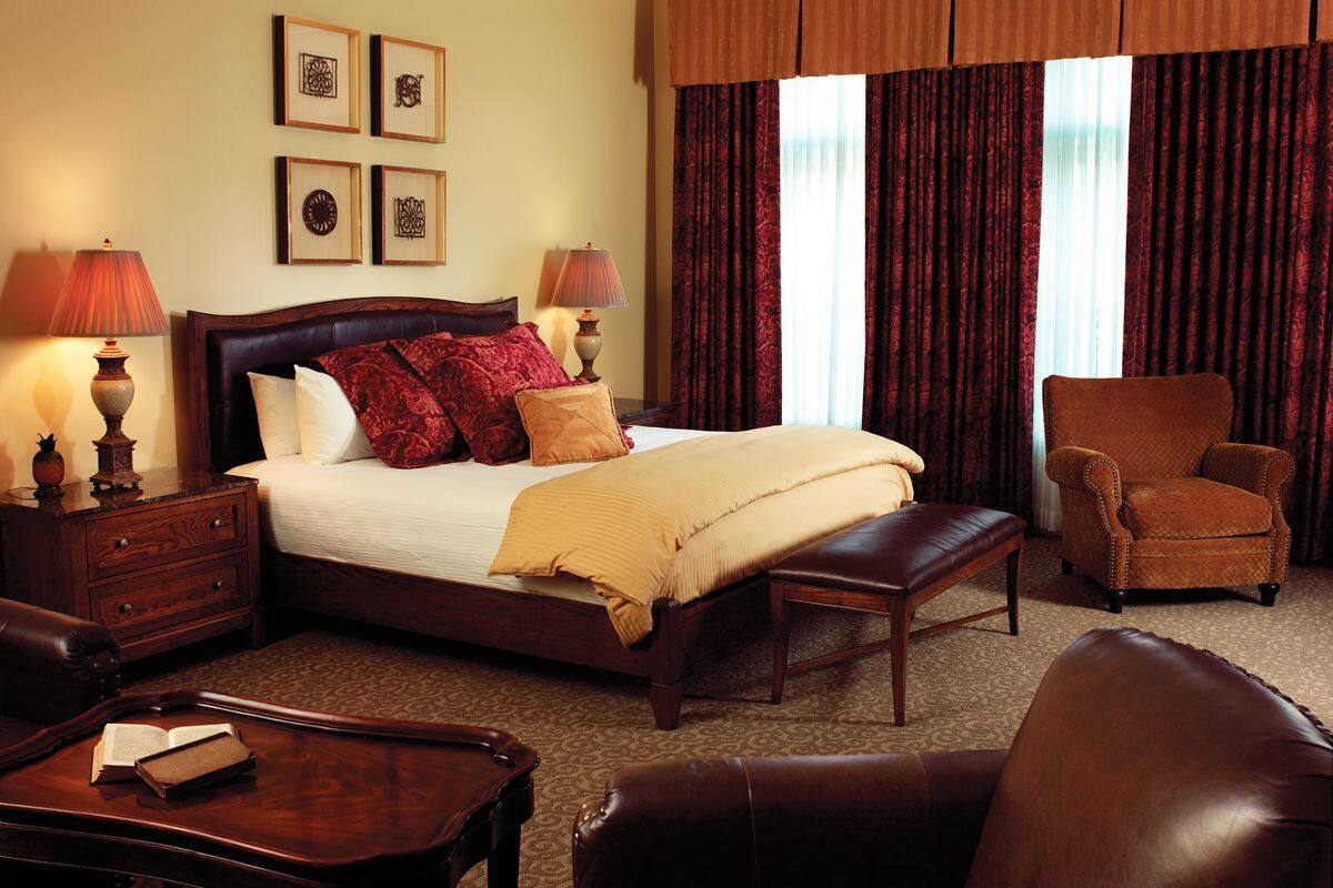 Habitación de hotel con una cama grande, dos mesitas de noche con lámparas, una silla, un sofá y suelo alfombrado.