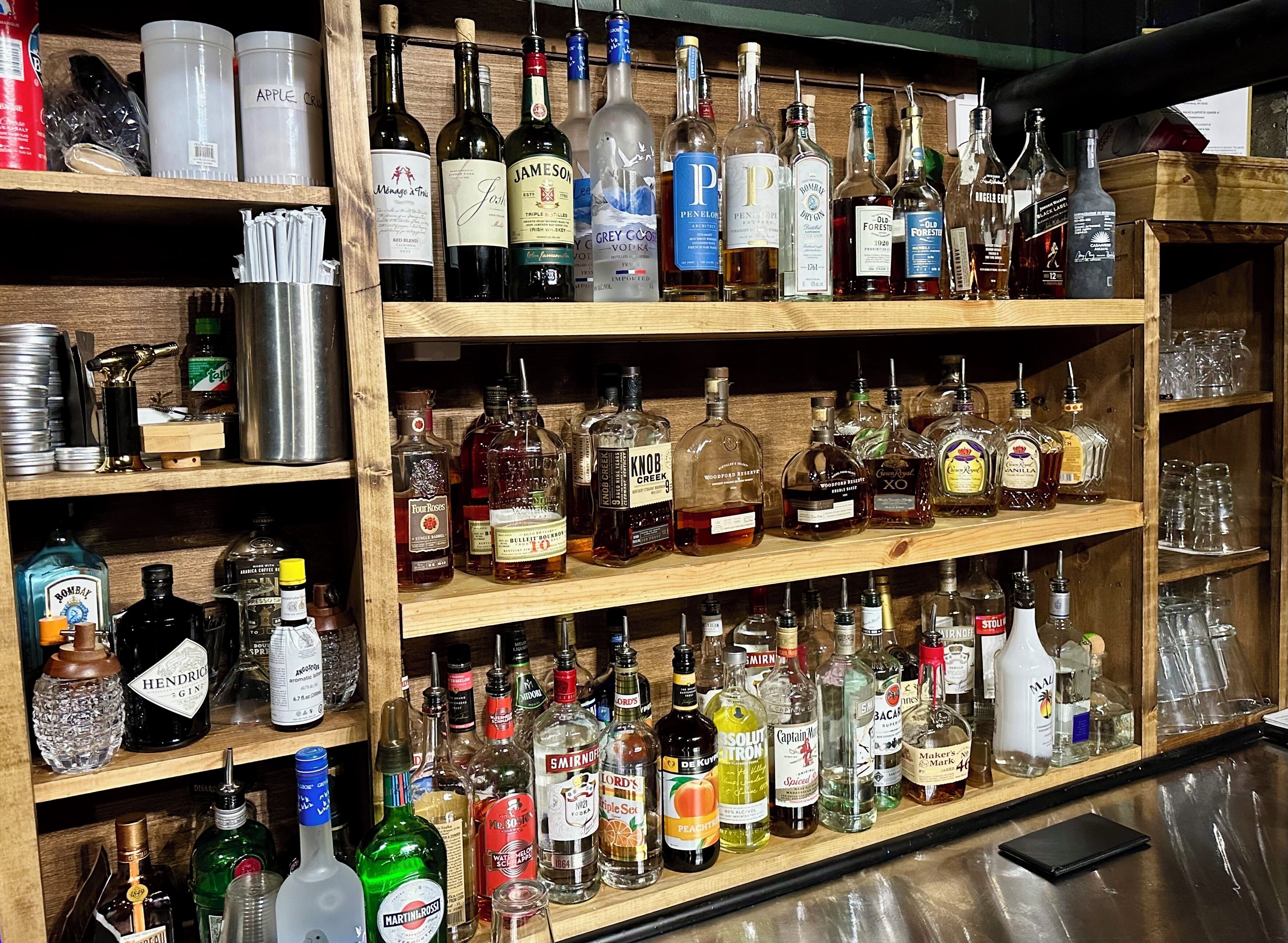A bar with shelves stocked with various bottles of alcohol, glasses, and bar tools.