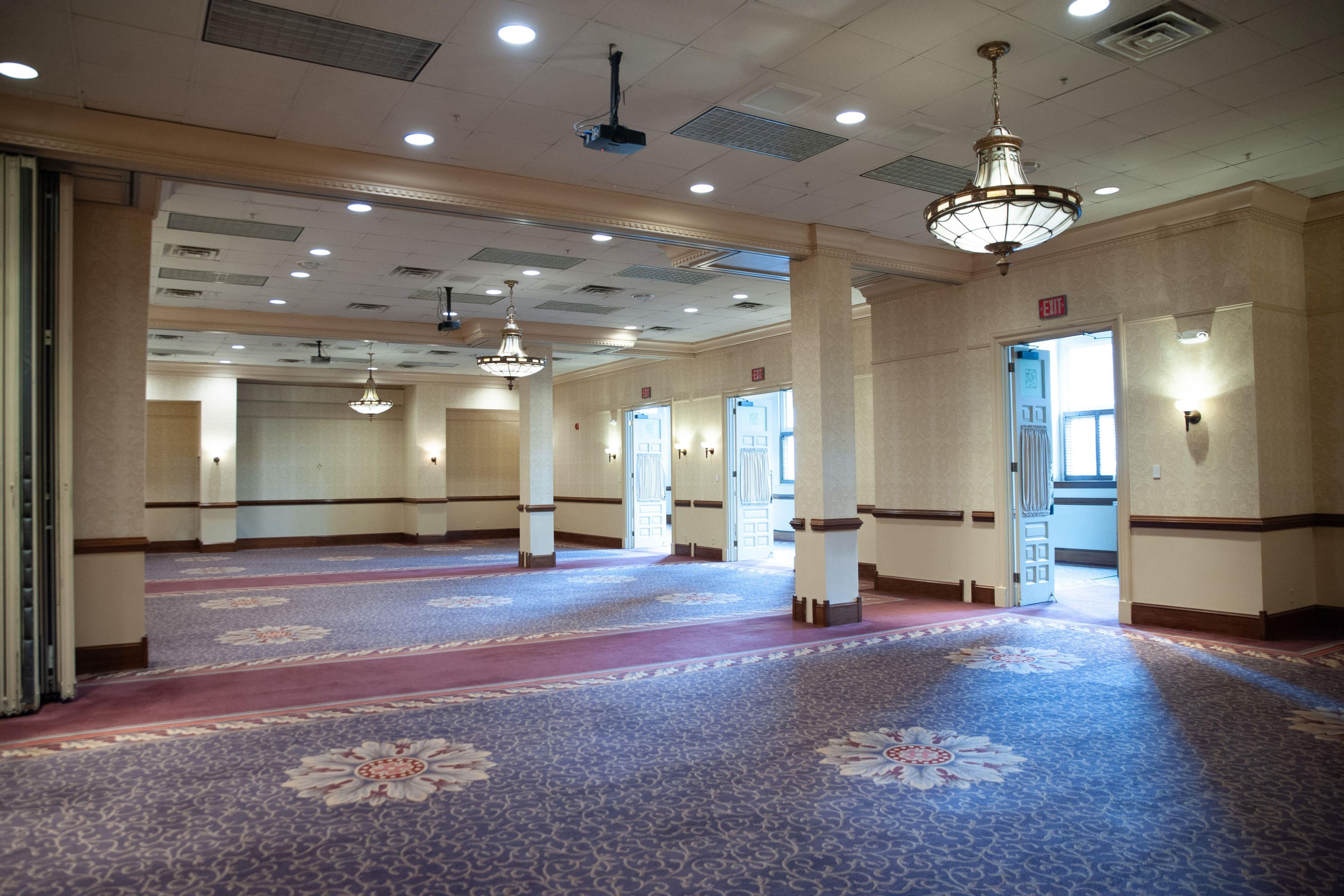 Un amplio vestíbulo de hotel con alfombra estampada, varias puertas y candelabros colgantes.