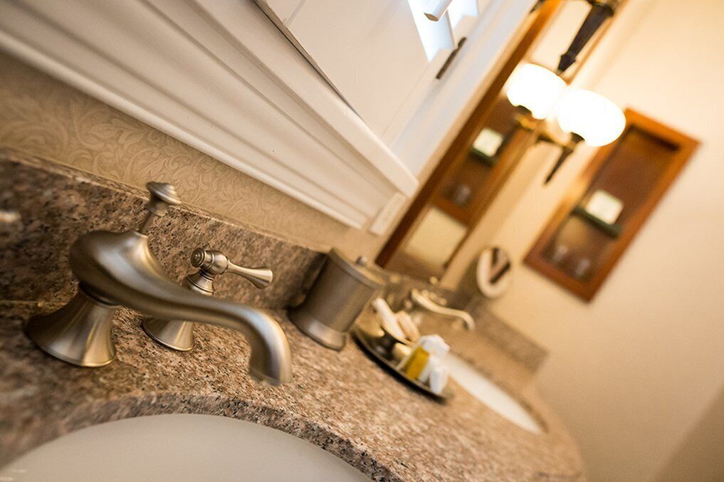 Un baño con encimera de granito, un lavabo, un espejo y una lámpara.