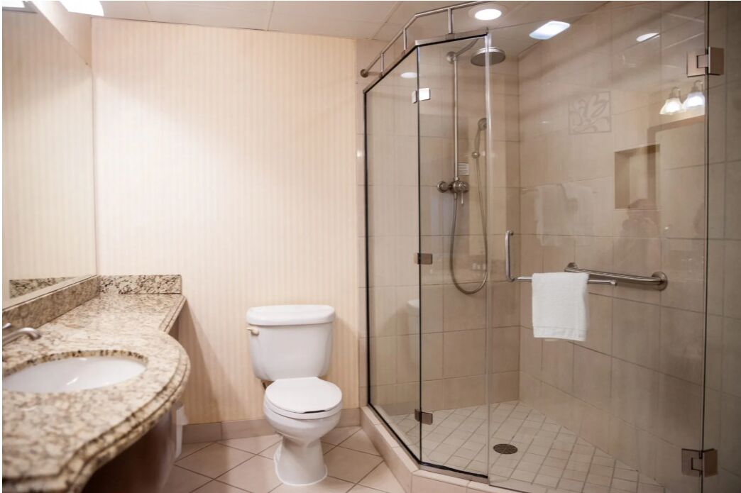 A bathroom with a granite countertop sink, a white toilet, and a glass-enclosed shower area.