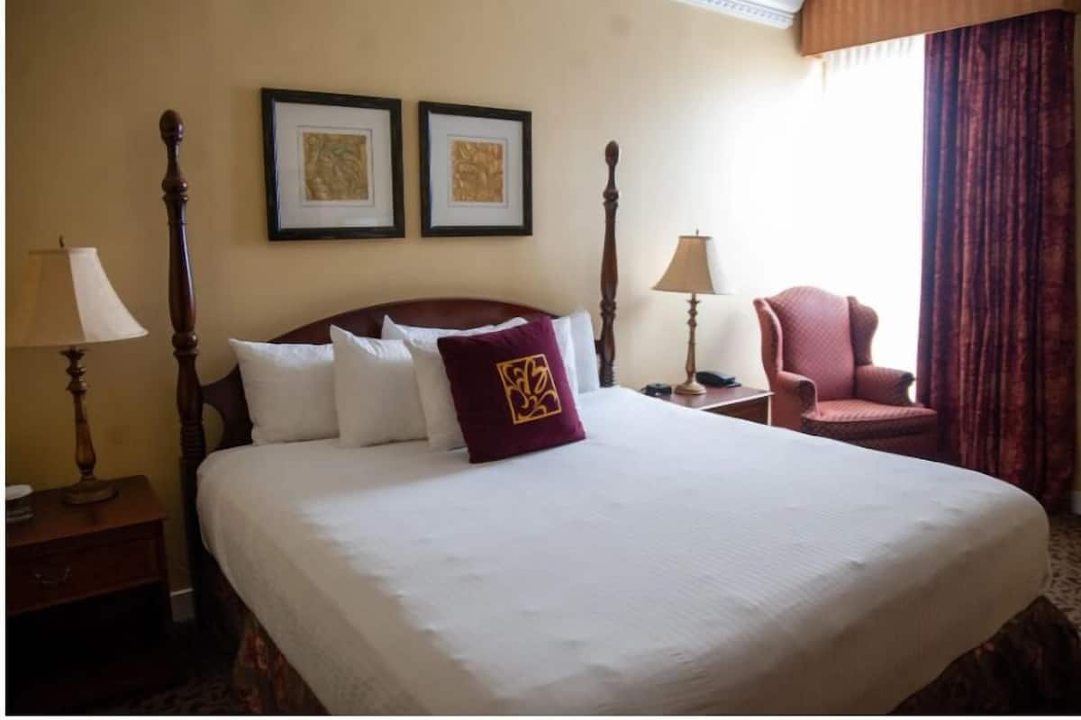 Una cama bien hecha con una colcha blanca grande y una almohada decorativa, flanqueada por dos mesitas de noche con lámparas.