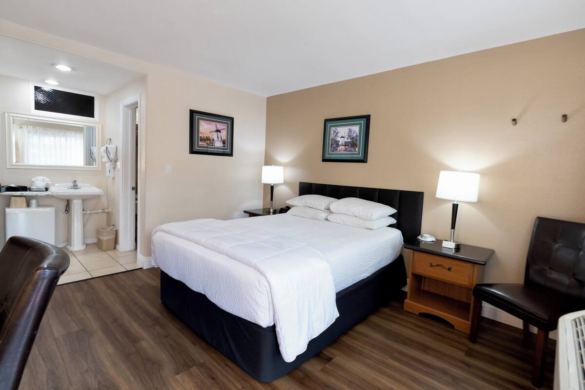 A hotel room with a large bed, a desk, a chair, a vanity with a mirror, and two framed pictures on the wall.