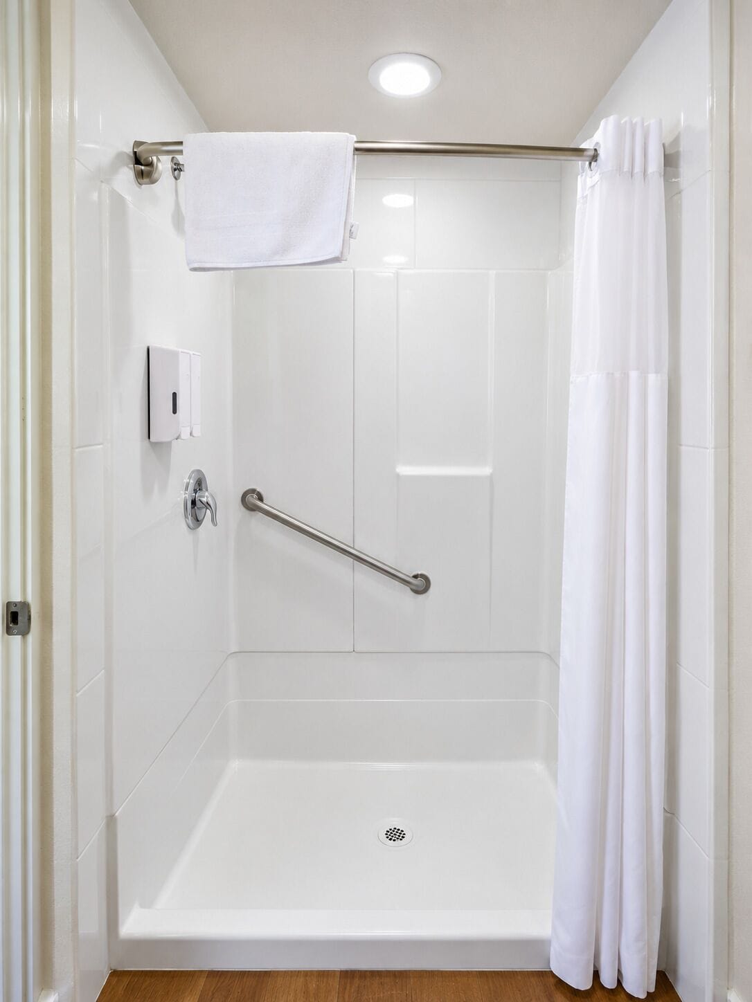 A white shower stall with a grab bar, a towel rack, and a shower curtain.