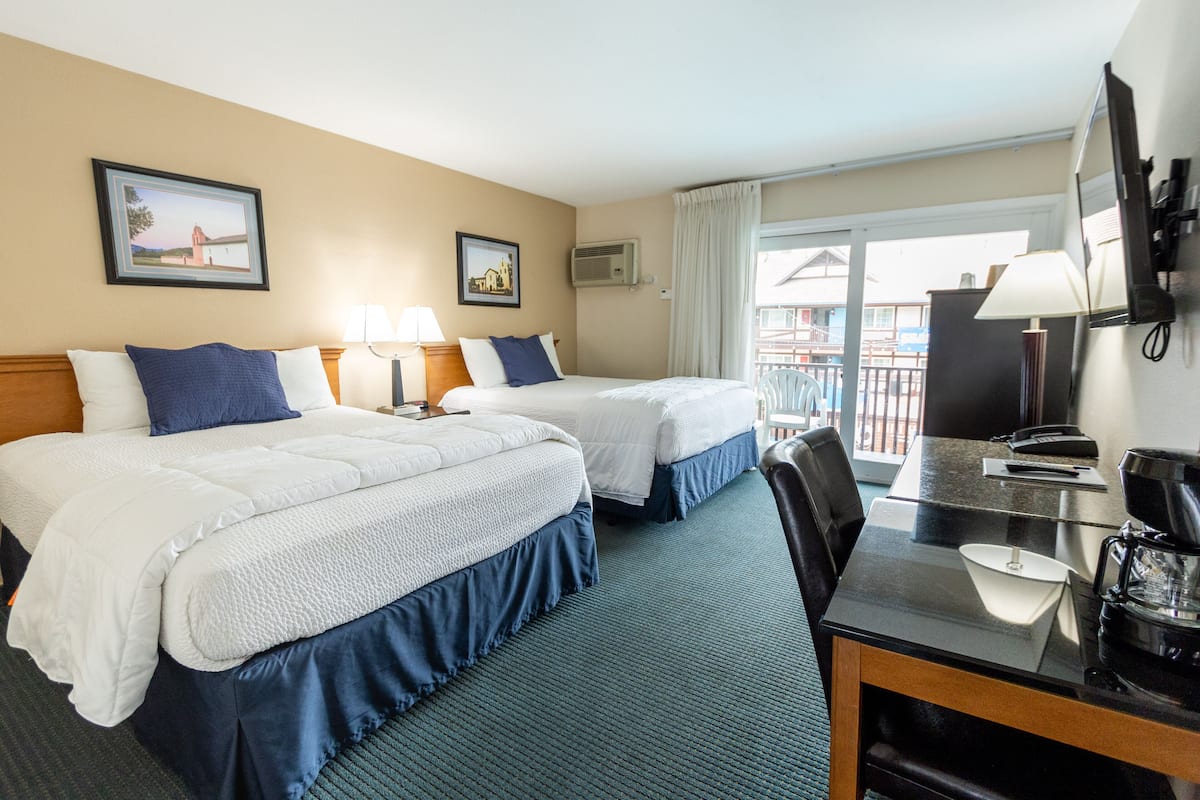 A hotel room with two beds, a desk, a chair, a TV, and a balcony with a view.