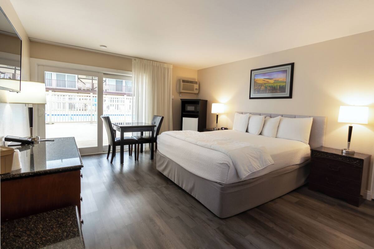 A hotel room with a bed, desk, chair, and a view of a balcony.
