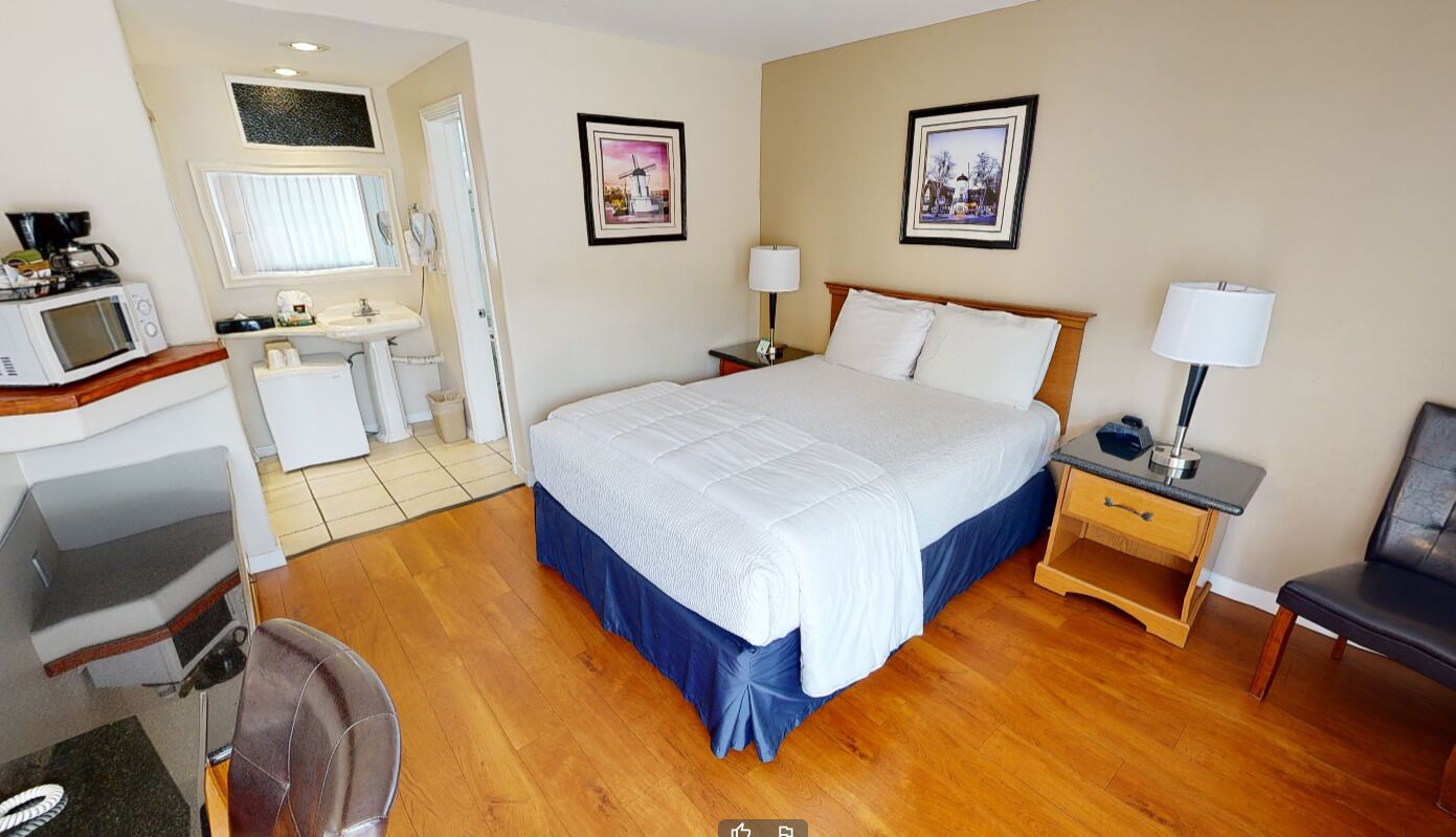 A hotel room with a bed, bedside tables, a desk with a chair, a microwave, and a sink.