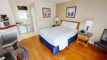 A hotel room with a bed, bedside tables, a desk with a chair, a microwave, and a sink.