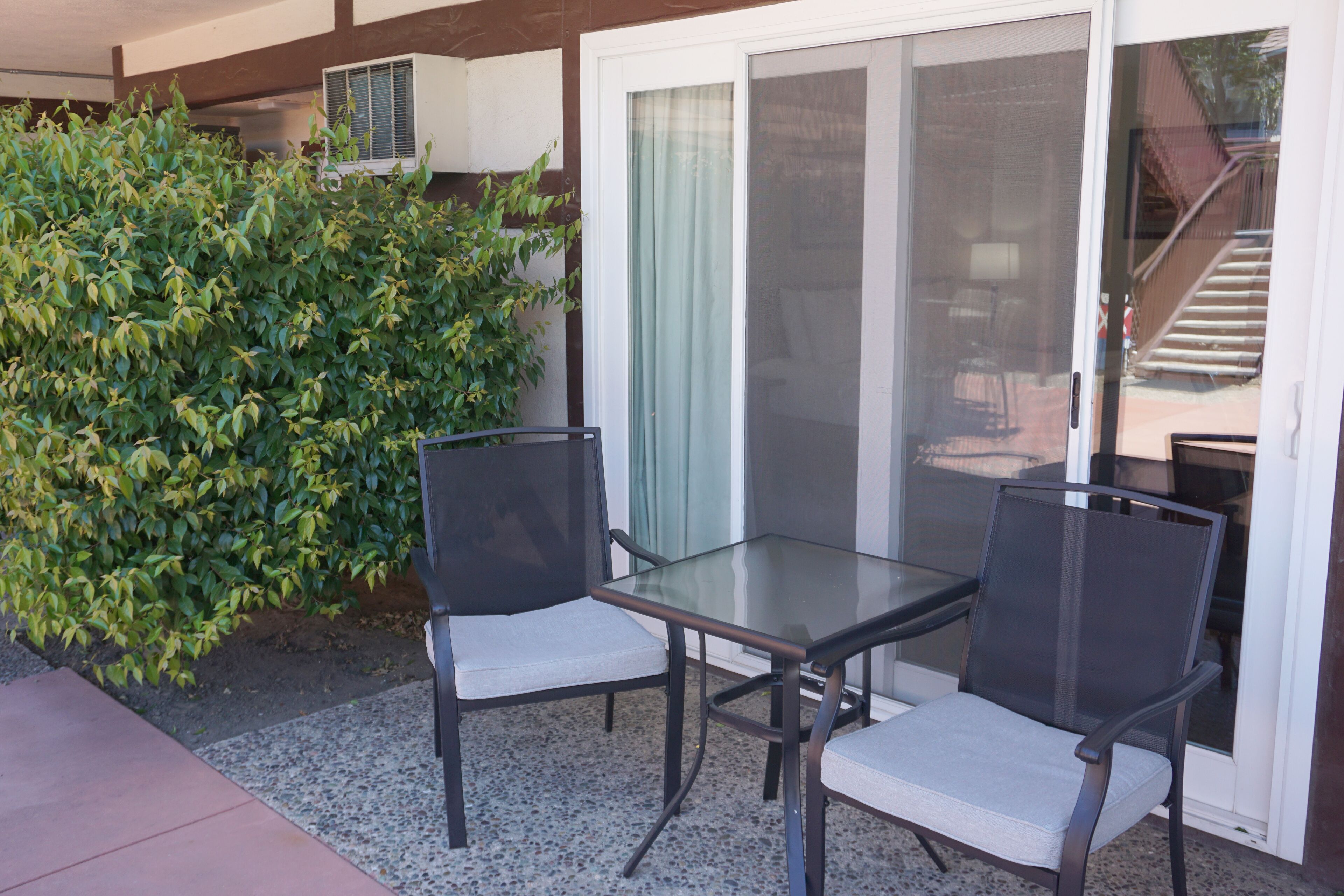 A patio area with two chairs and a table, a sliding glass door, and a green bush.