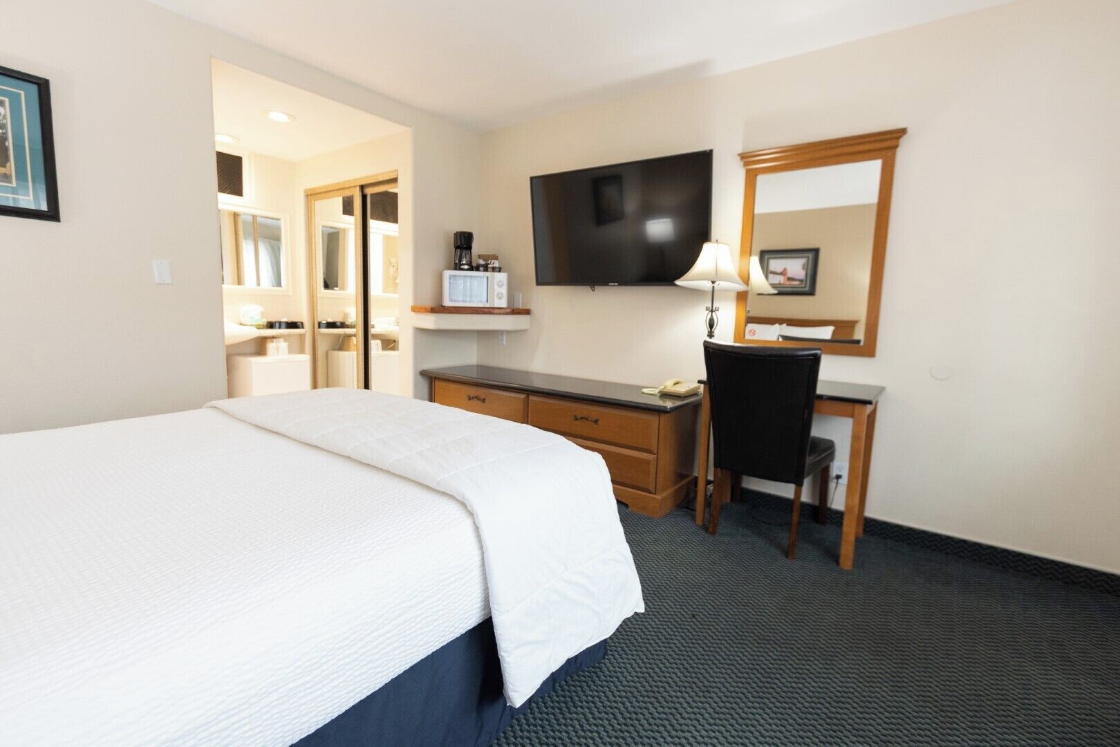 A hotel room with a bed, desk, chair, television, and a mirror.