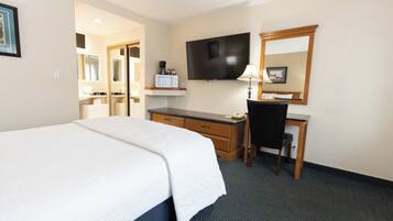 A hotel room with a bed, desk, chair, television, and a mirror.
