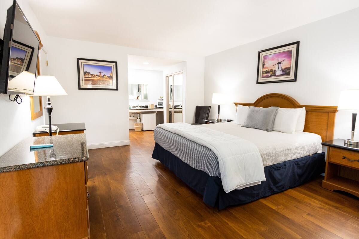 A hotel room with a bed, bedside tables, a desk, a chair, a mirror, and a television.