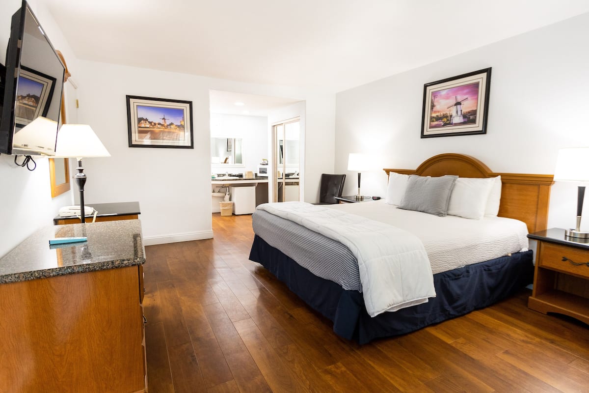 A hotel room with a bed, bedside tables, a desk, a chair, a mirror, and a television.