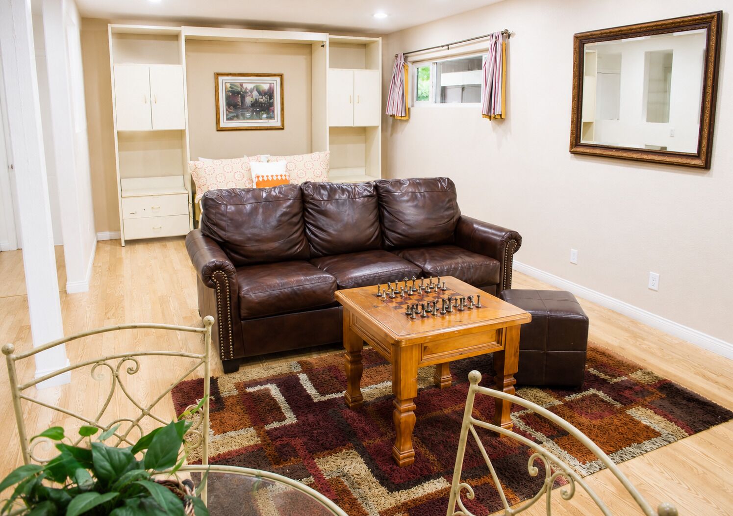 A living room with a brown leather sofa, a wooden coffee table with chess pieces, a patterned rug, and a metal chair.