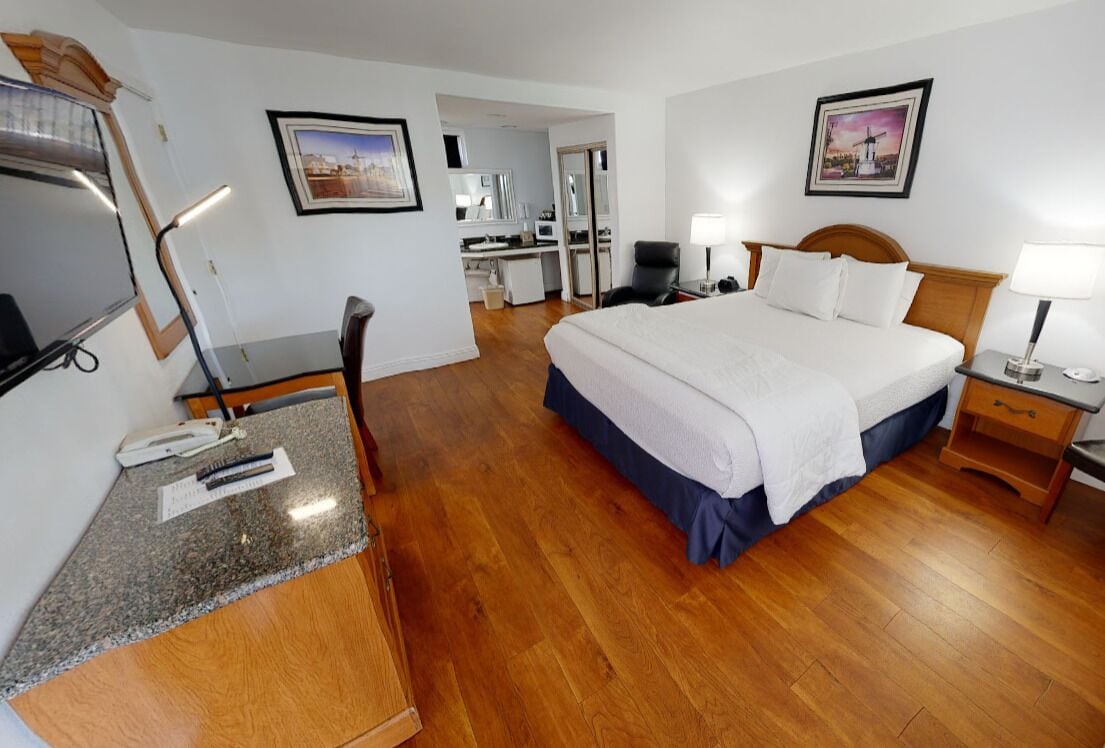 A hotel room with a bed, desk, chair, and a mirror.