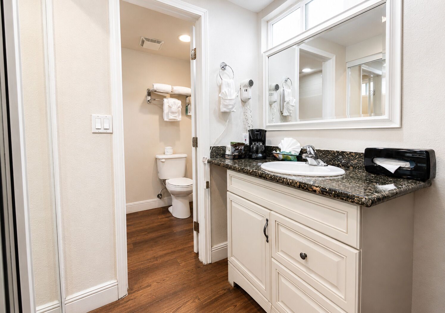 A bathroom with a white toilet, a sink with a granite countertop, and a mirror above the sink.