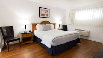 Une chambre d’hôtel avec un lit en bois, deux tables de chevet avec des lampes, une chaise, un tableau au mur et une fenêtre avec des rideaux.