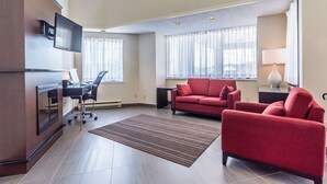 A spacious living area with a flat-screen TV mounted on the wall, a red sofa, a matching armchair, and a desk with a chair. - Comfort Inn Thetford Mines (Thetford Mines)