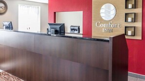 A hotel reception desk with a red wall, a clock, and a sign that reads "Comfort Inn". - Comfort Inn Thetford Mines (Thetford Mines)
