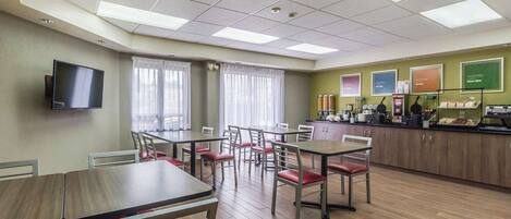Un espace repas avec des tables et des chaises, un comptoir de cuisine équipé d’appareils électroménagers et un téléviseur fixé au mur.