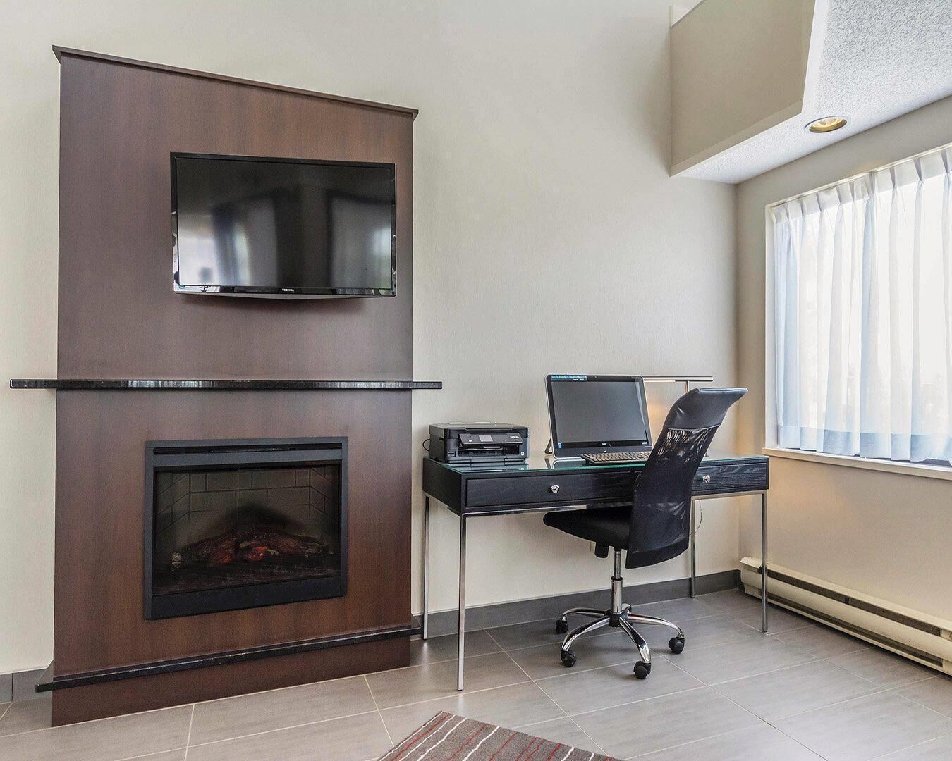Un espacio de oficina moderno con chimenea, un escritorio con una computadora portátil y un televisor montado en la pared.