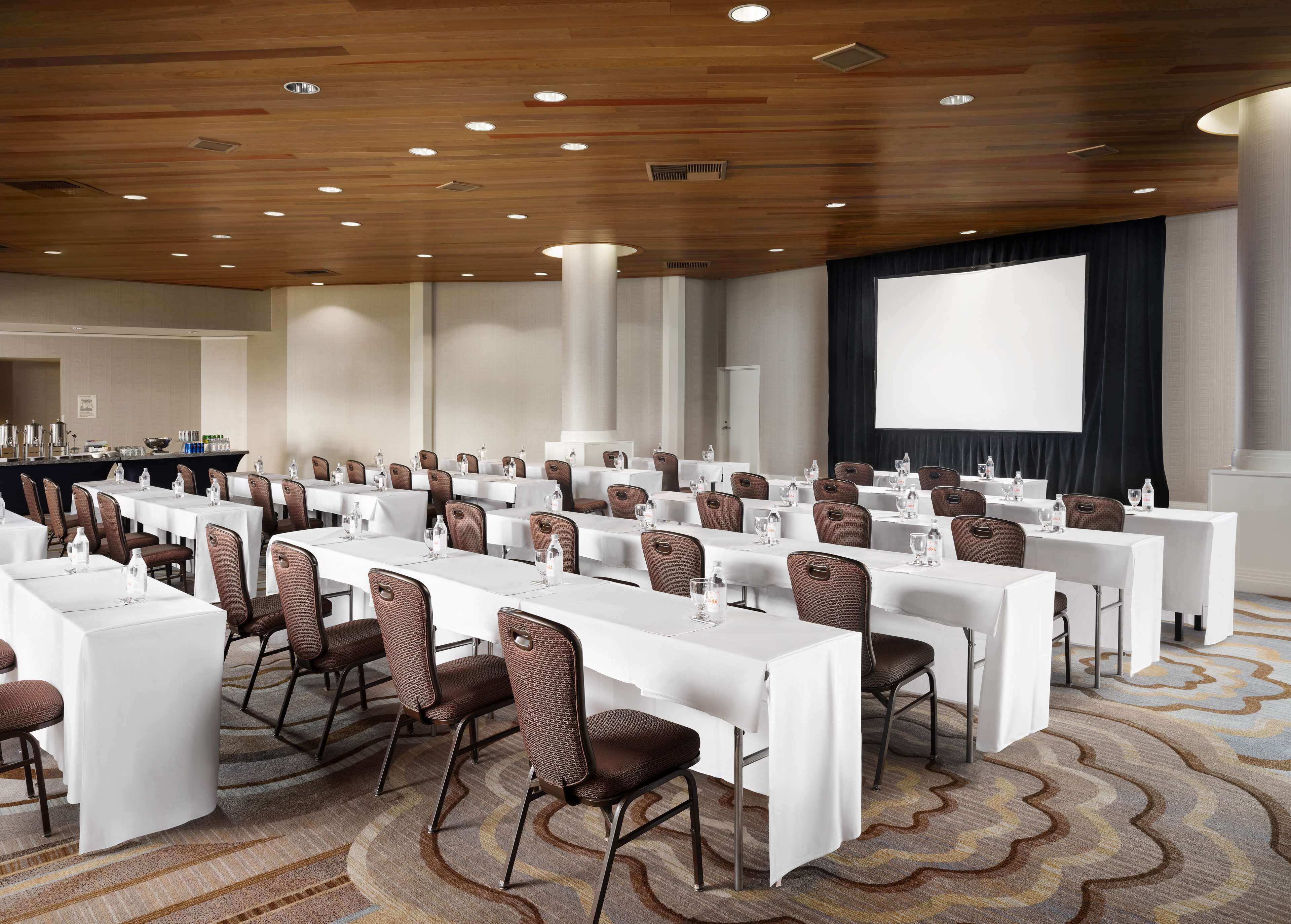 Un salón de conferencias con varias mesas y sillas, una pantalla de proyector y una zona de bar.