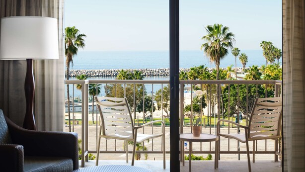 Une chambre d’hôtel avec balcon donnant sur une plage, comprenant un lit, une lampe et deux chaises.