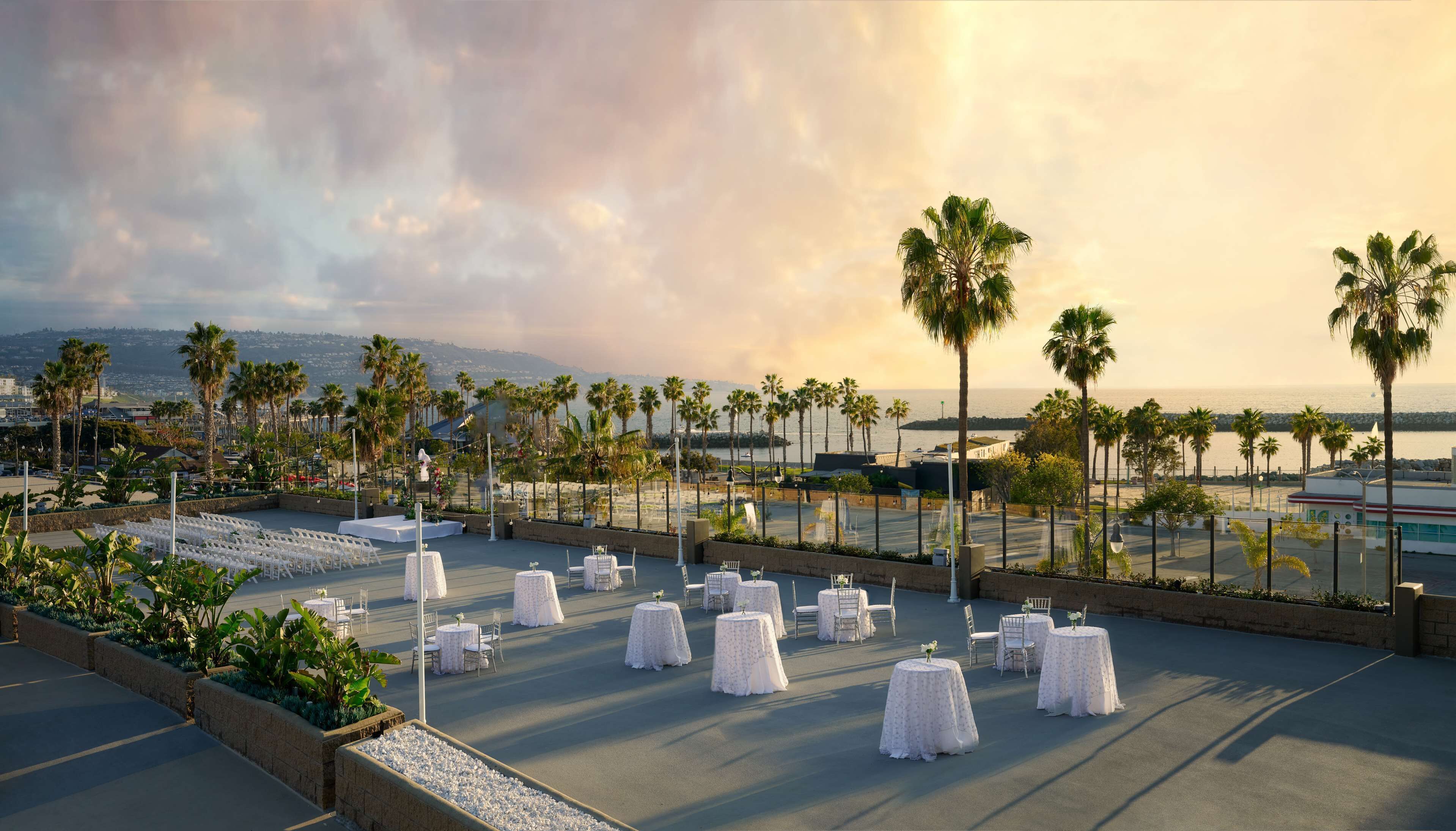 Een dakterras met tafels klaar voor een evenement, met uitzicht op een strand en stadsbeeld.