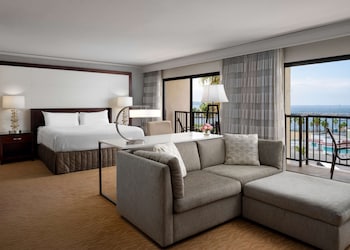 A spacious dining area with multiple wooden tables and chairs, large windows, and a modern ceiling design. at Sonesta Redondo Beach & Marina