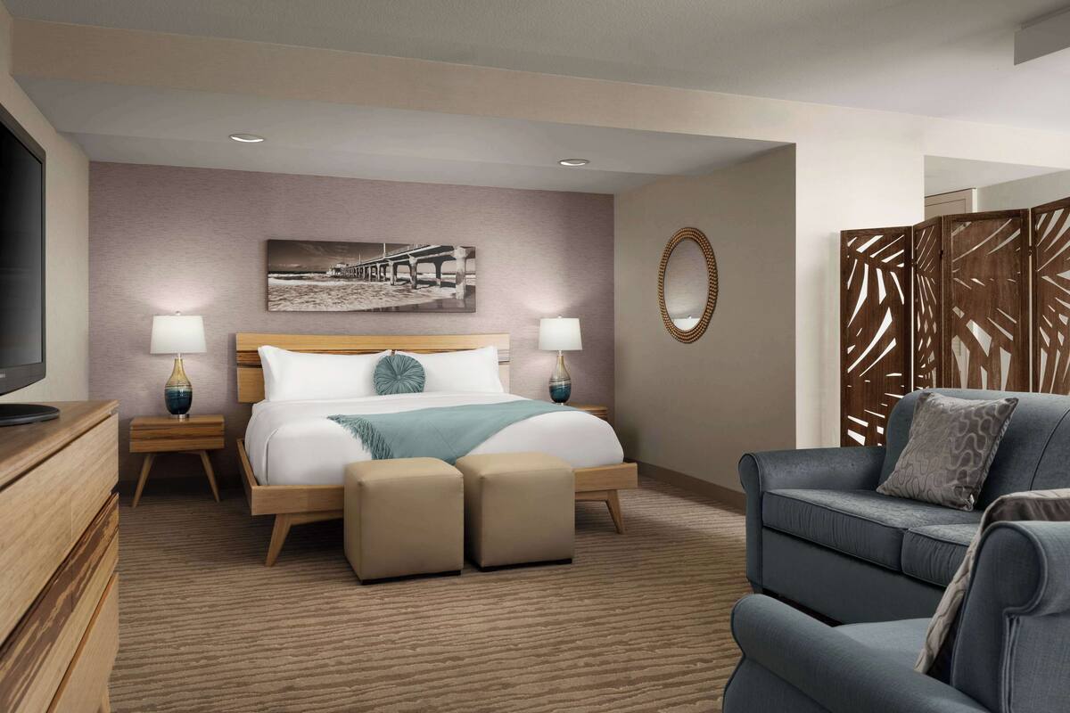 Une chambre d’hôtel moderne avec un grand lit, deux tables de chevet avec des lampes, une télévision, un canapé et un élément décoratif mural.